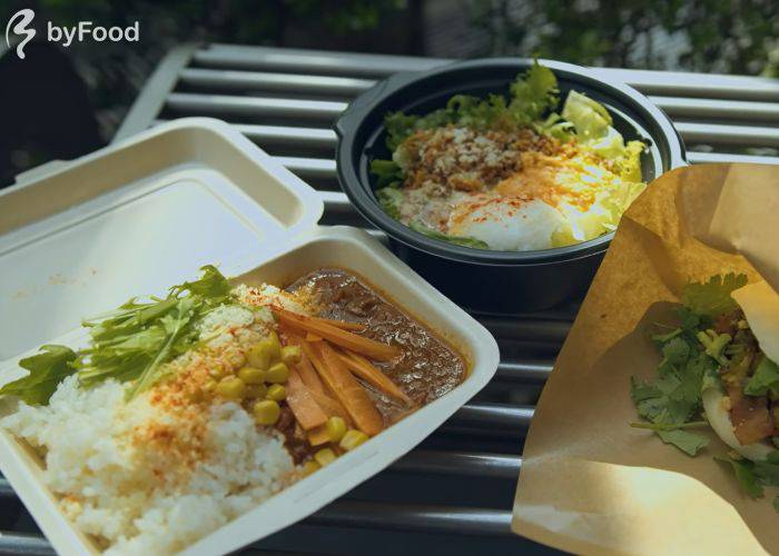 Vegan curry, taco rice and a bao bun on a bench, purchased from nearby food trucks in Tokyo.